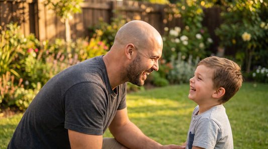 A bald dad laughing with his young child outdoors in the backyard, Father's Day gift guide for bald dads