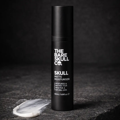 Black moisturizer bottle with 'The Bare Skull Co.' branding on a dark background
